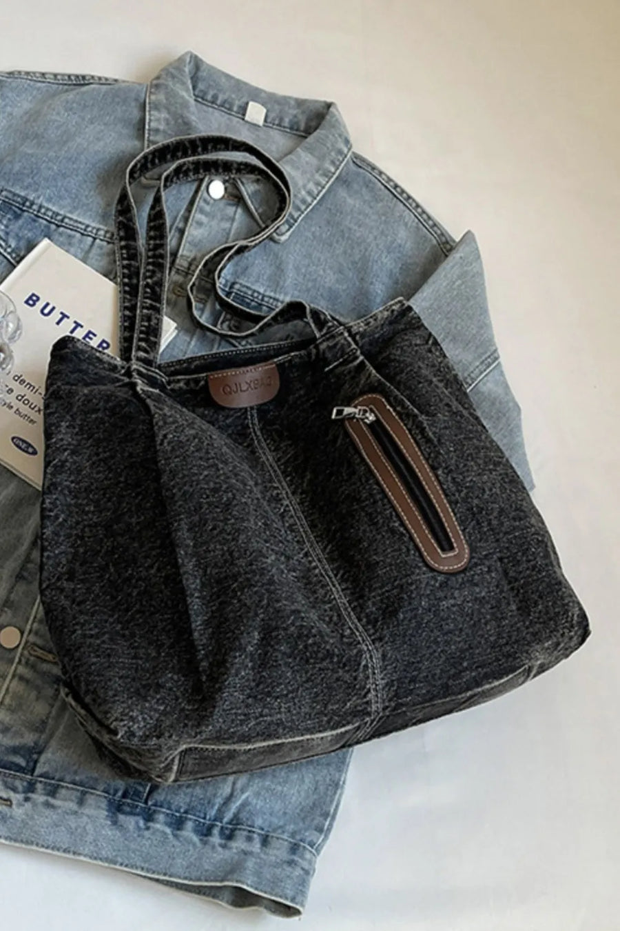 Dark denim tote bag with leather trim and zippered pocket detail.