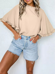 Apricot ruffled mock neck shirt with half sleeves and bell cuffs, paired with denim shorts.