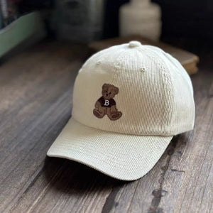 White corduroy baseball cap with embroidered teddy bear detail.