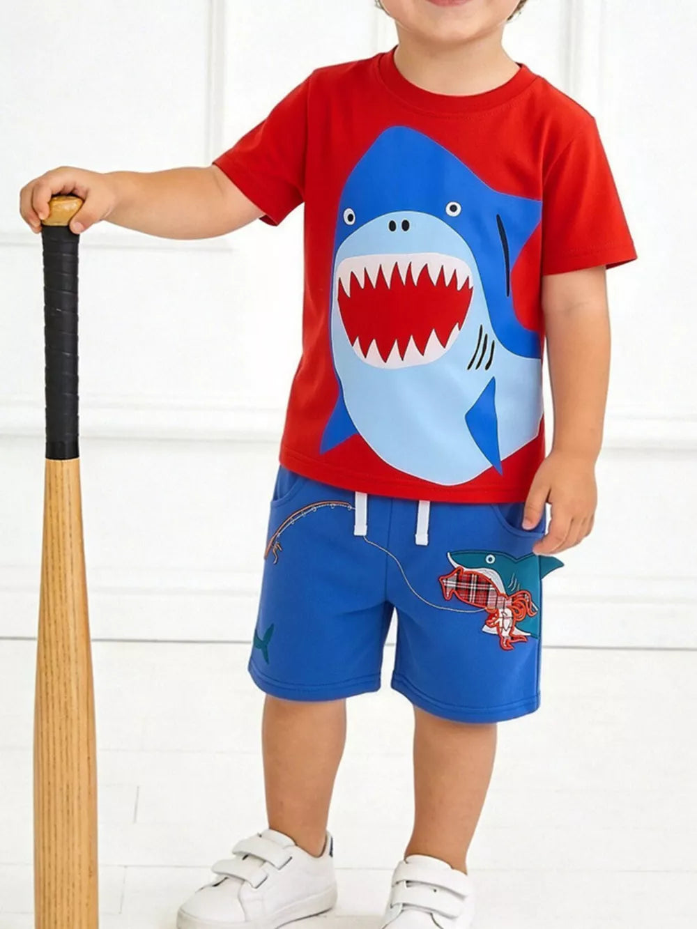 Toddler red cotton t-shirt with shark graphic and blue shorts with shark embroidery.