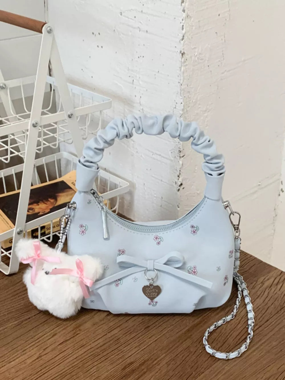 Blue ruched mini crossbody bag with floral print, bow charm, and fluffy pom pom keychain.