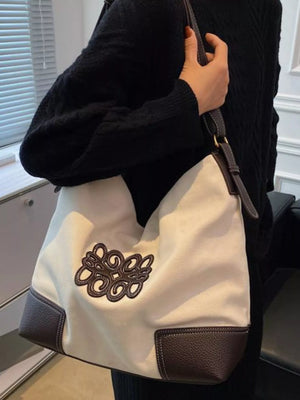 White canvas tote bag with brown leather trim and embroidered logo detail