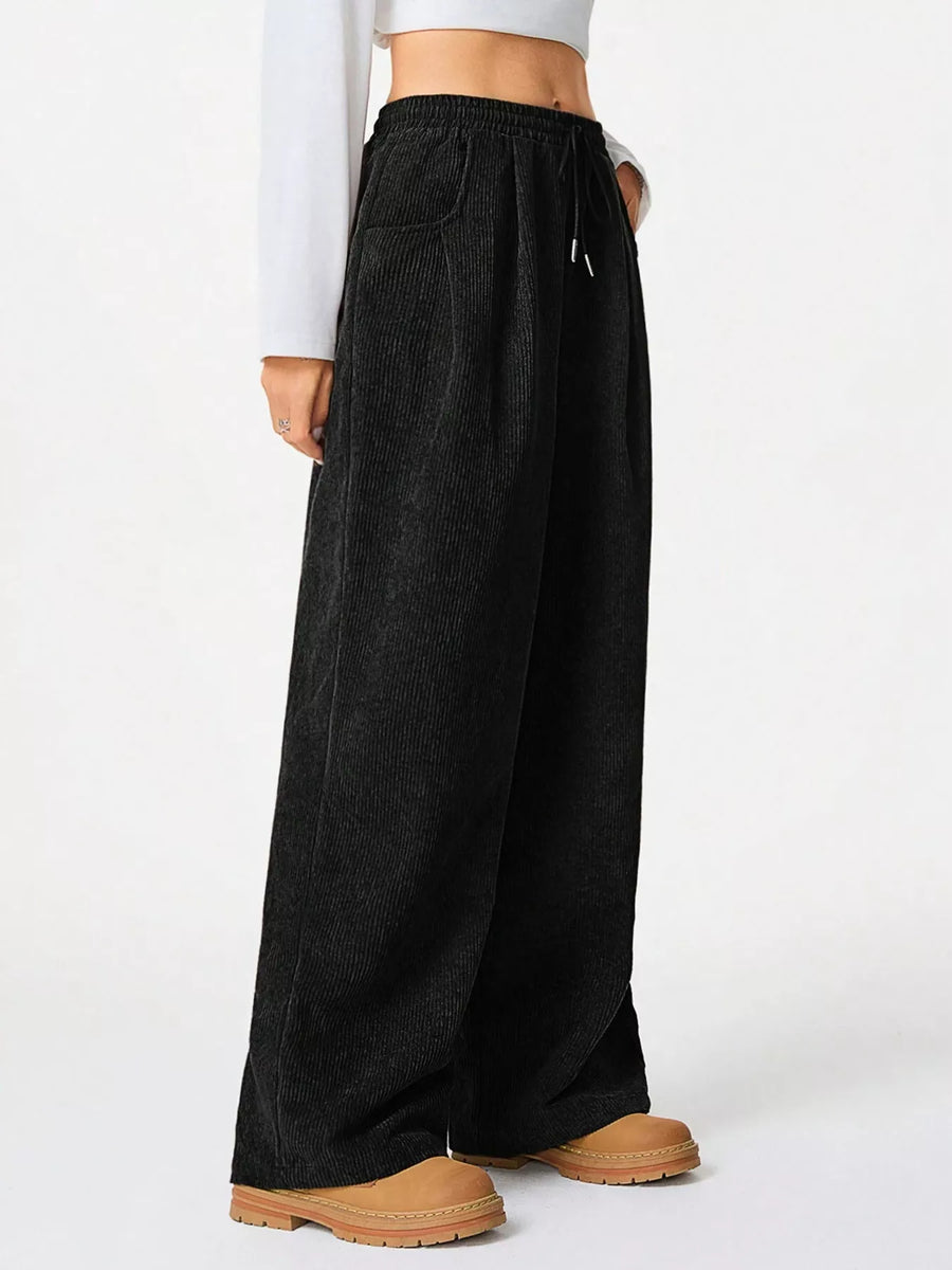Black corduroy pants with drawstring waist and wide leg, styled with a white top.