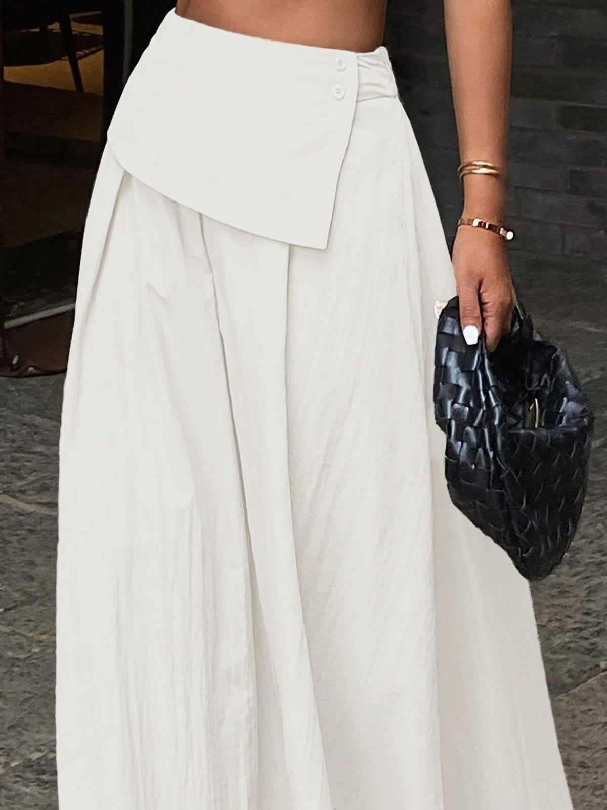 Pleated high-waisted maxi skirt in white with a button detail and a draped overlay.