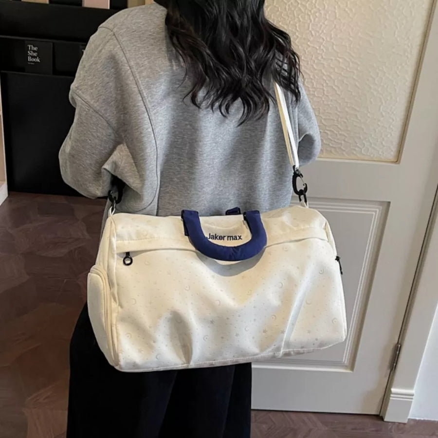 Cream white duffel bag with crescent moon and star pattern, adjustable strap, and blue handles.