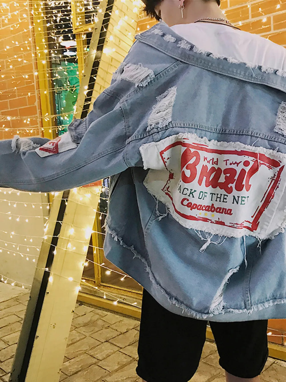 Men's light wash distressed denim trucker jacket with Brazil graphic patch and frayed hem.