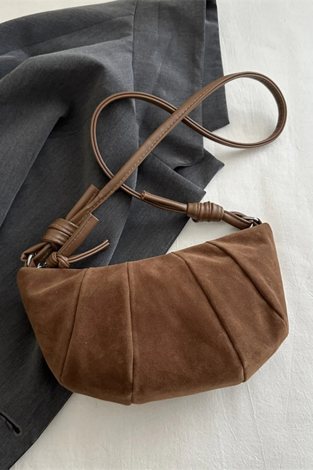 Brown suede crescent shoulder bag with pleated detail and knotted strap.