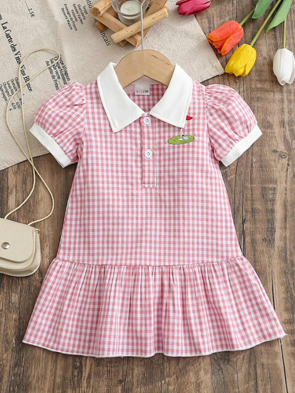 Baby girl's pink gingham polo dress with white collar, cuffs, and ruffle hem.