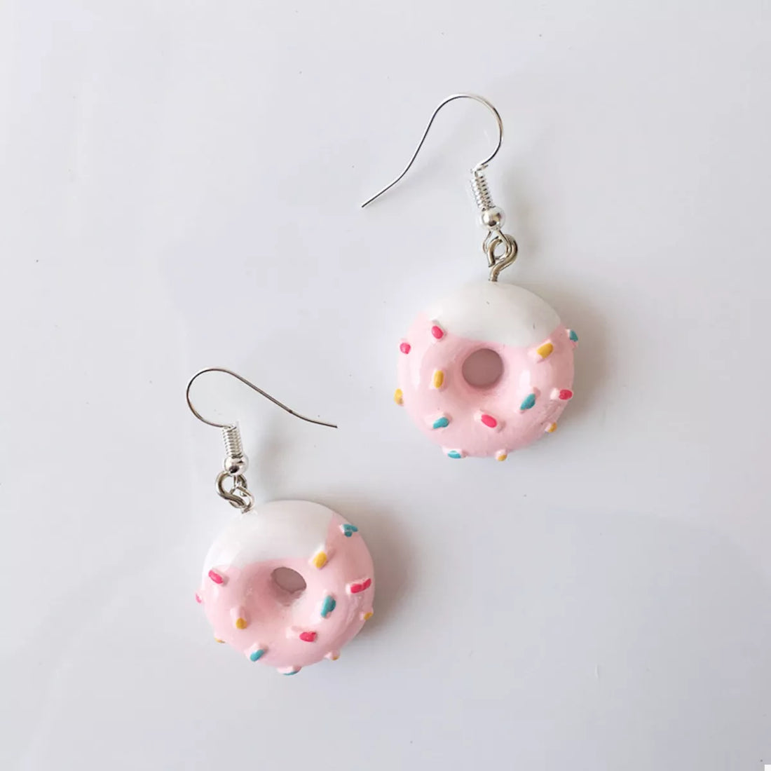 Pink donut dangle earrings with white icing and colorful sprinkles.