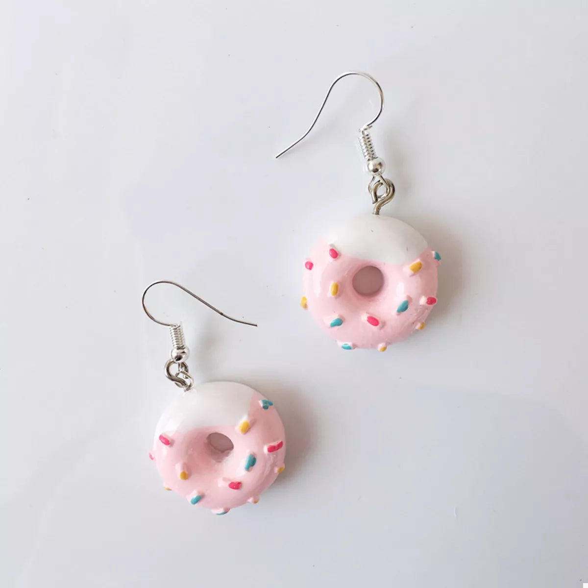 Pink donut dangle earrings with white icing and colorful sprinkles.
