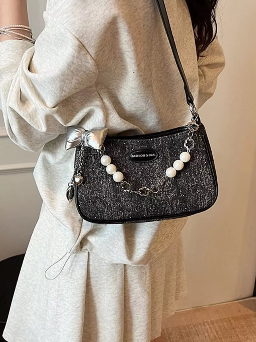 Black shoulder bag with pearl chain, silver bow and clover charm.
