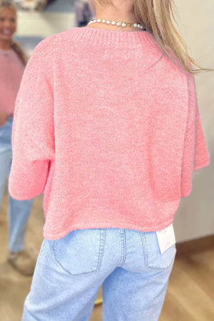 Pink acrylic knit boxy cardigan with button front, crew neck, and short sleeves.