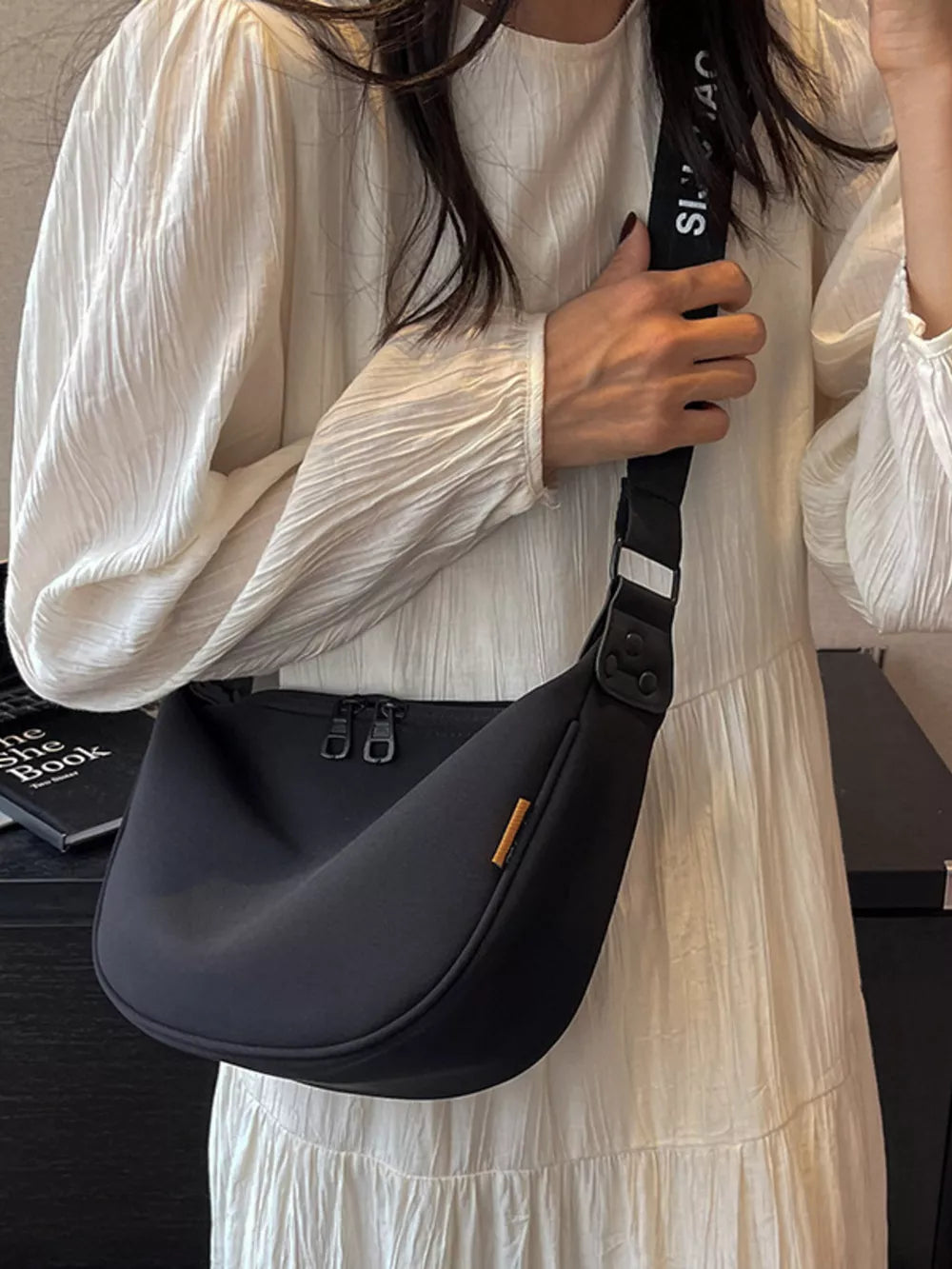 Black crescent crossbody bag with adjustable strap and double zipper.