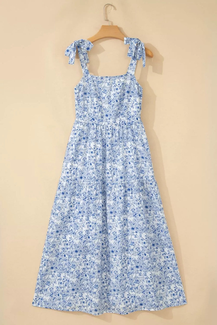 Maxi dress with blue floral print, square neck, tie straps, and tiered skirt.