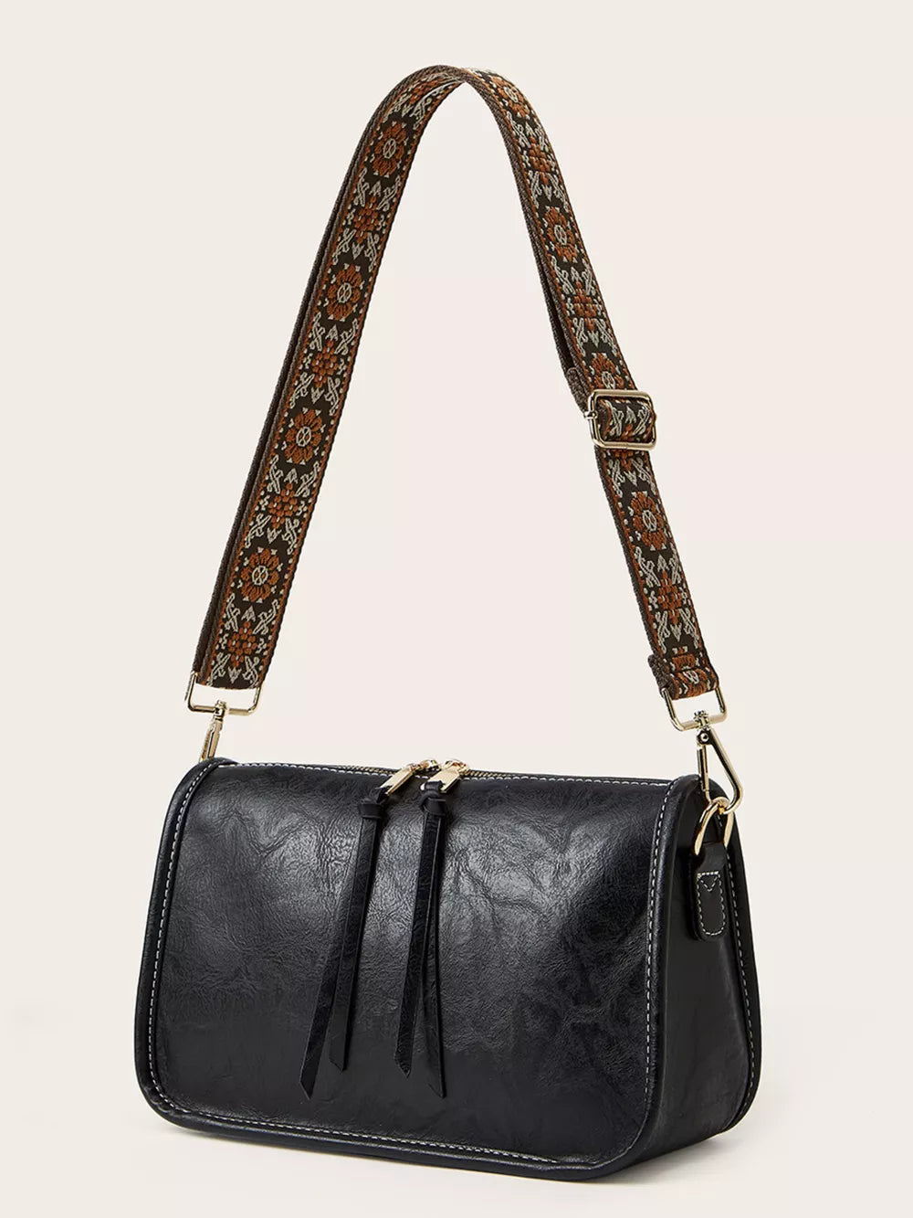 Black crossbody bag with adjustable patterned strap and tassel zipper pulls