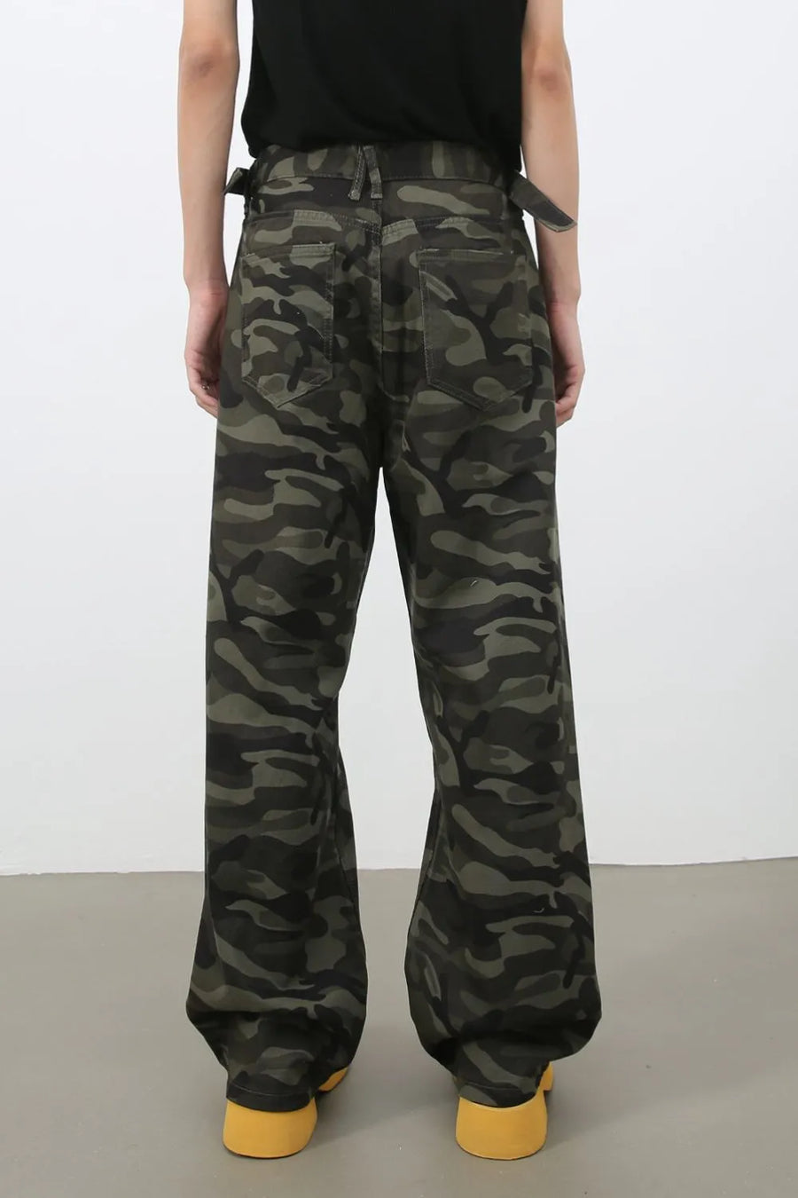 Wide-leg camo denim trousers in black with adjustable waist straps and yellow shoes.