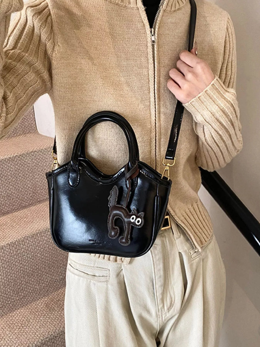 Black patent leather mini crossbody bag with a playful brown cat charm.
