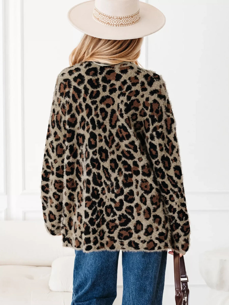 Leopard print fuzzy cardigan with long sleeves and pockets, styled with jeans and a hat.