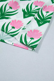White polyester blouse with pink floral and green leaf print, showing hem detail.