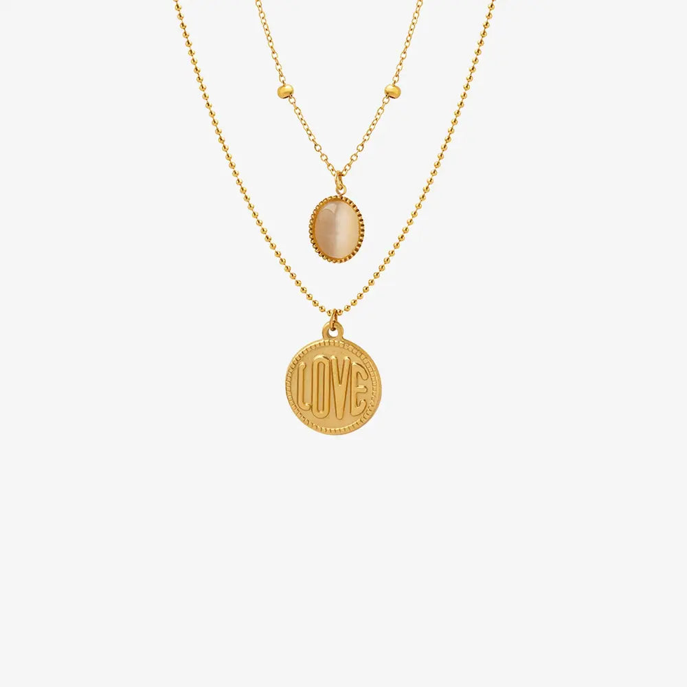 Gold layered necklace with beaded chain, oval stone, and round love coin pendant.