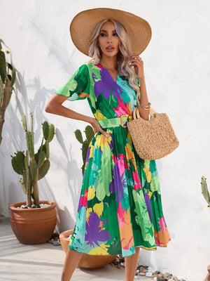 Tropical pleated midi dress in dark green with a vibrant floral print and matching belt.