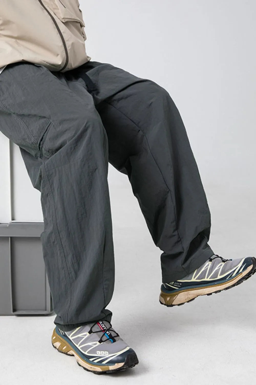 Dark gray technical fabric cargo pants with belt detail and large pockets.