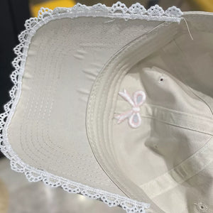 Beige baseball cap with embroidered bow detail and white lace trim.