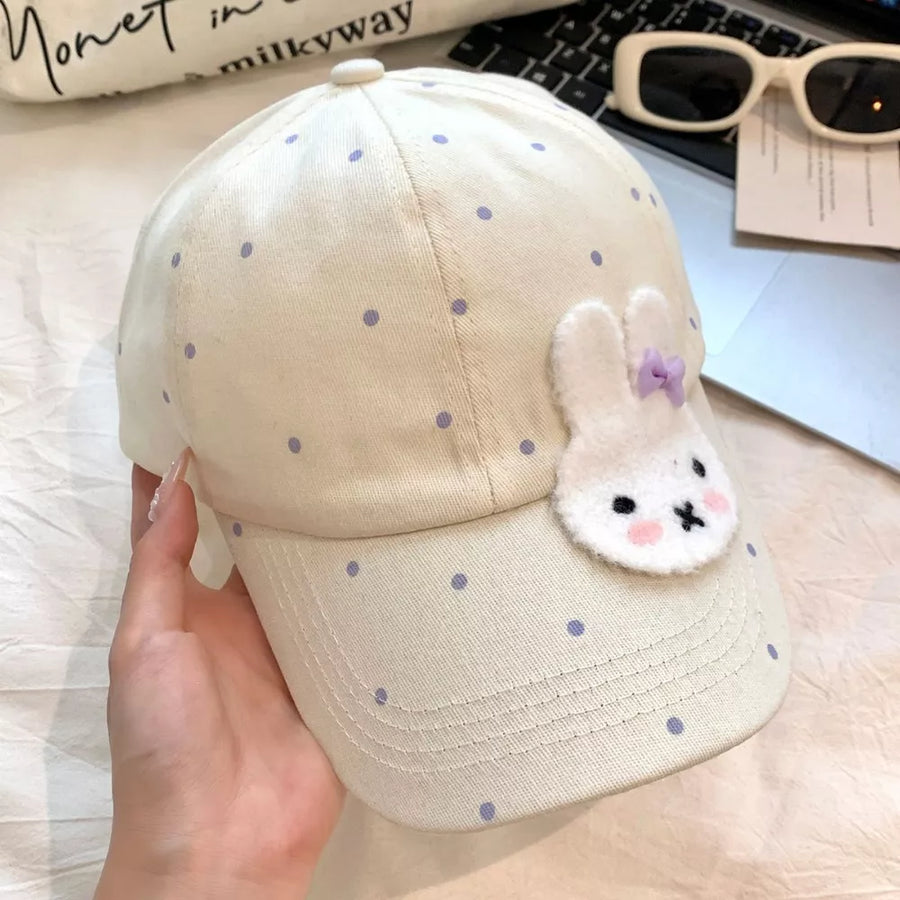 Ivory polka dot baseball cap with white bunny applique and purple bow.