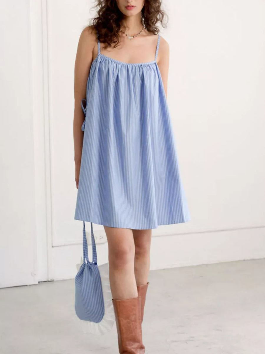 Blue striped mini dress with spaghetti straps and tie details, paired with brown boots.