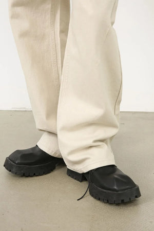 Oversized beige denim jeans with a sculpted leg, shown with black chunky sole shoes.