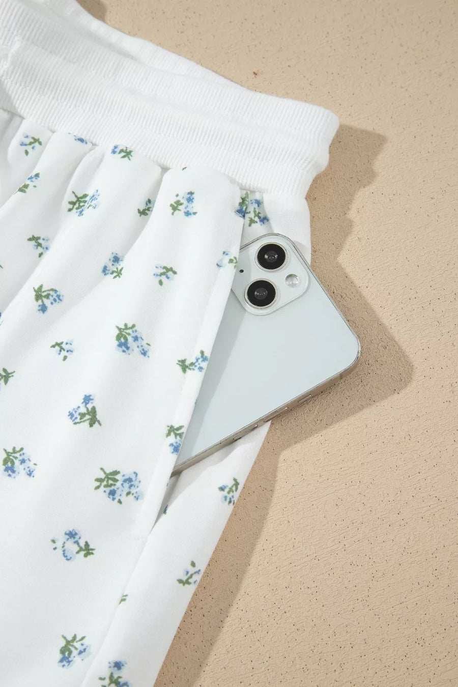 White floral print sweatpants with a drawstring waist and a side pocket holding a phone.