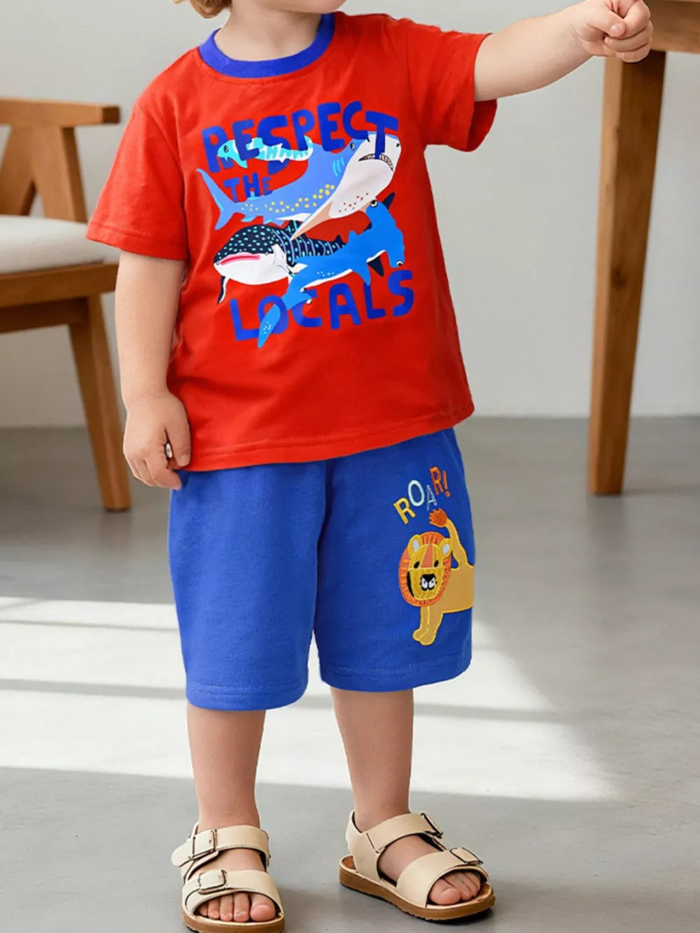 Children's red t-shirt with blue shark graphic and text, blue shorts with lion graphic.