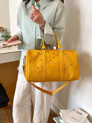 Yellow crocodile textured duffel bag with studded details and detachable strap.