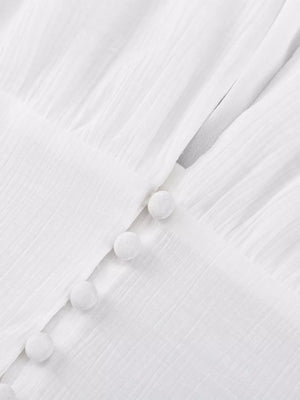 White textured fabric dress with pom pom buttons and a V-neckline detail.