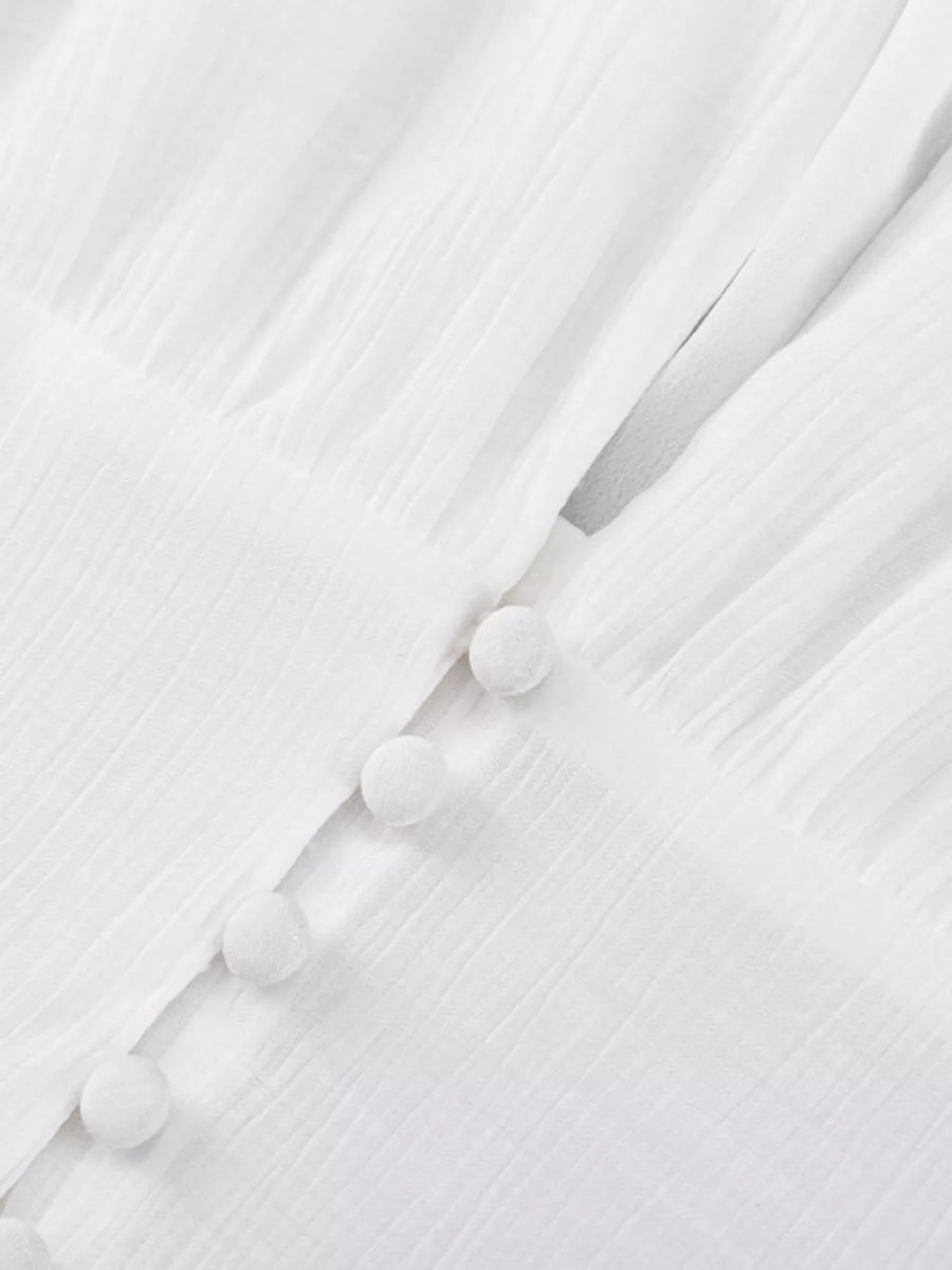 White textured fabric dress with pom pom buttons and a V-neckline detail.