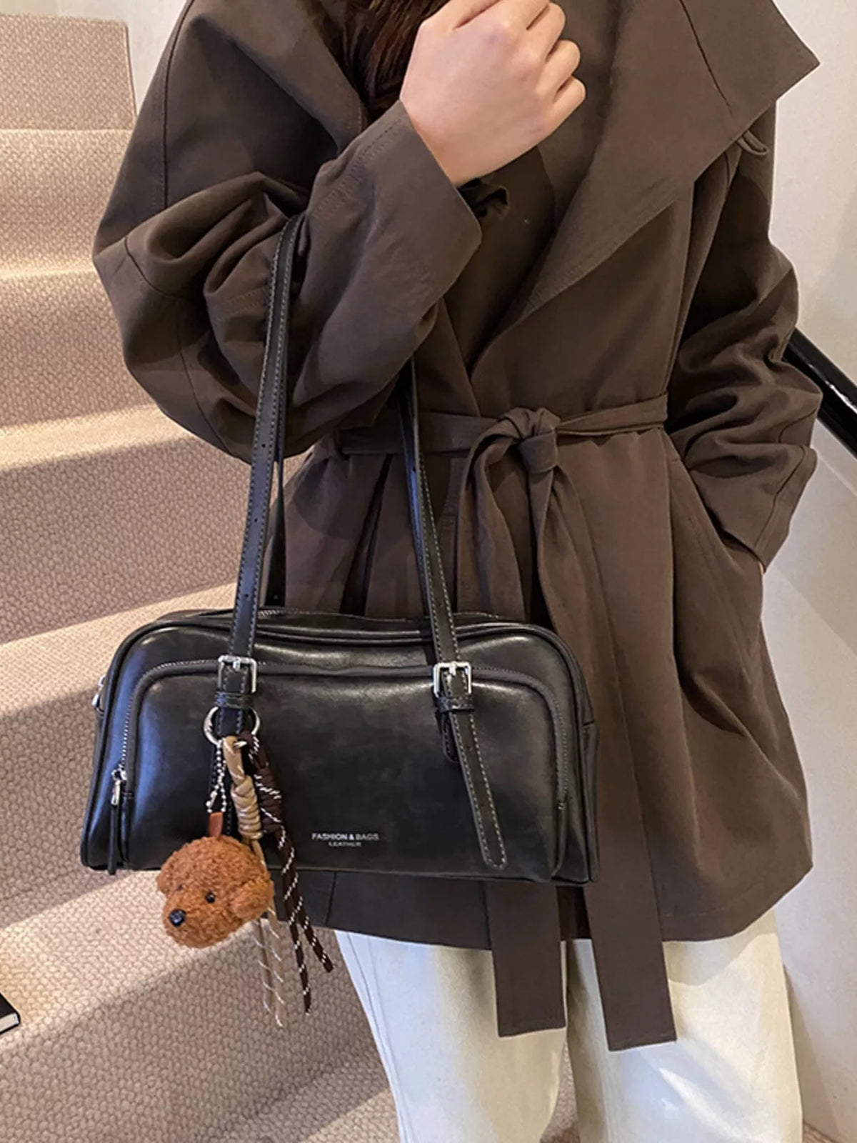 Black leather shoulder bag with buckle details and a teddy bear charm.