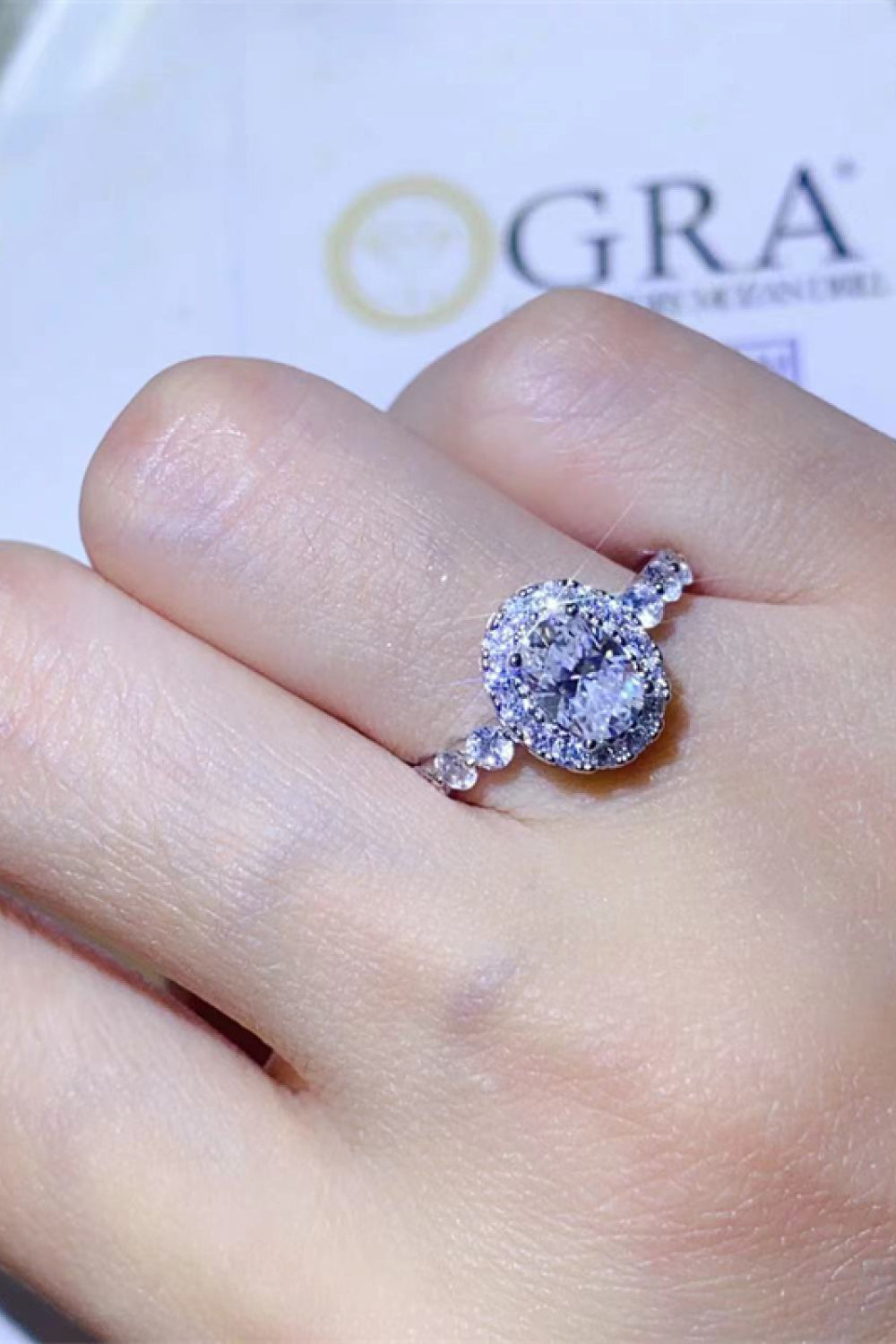 White oval moissanite halo ring with diamond band on hand