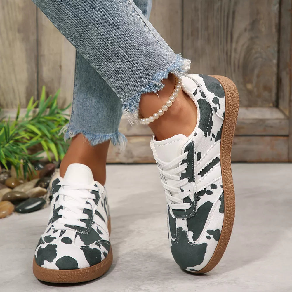 Trendy cow print low-top sneakers with white laces and brown soles.