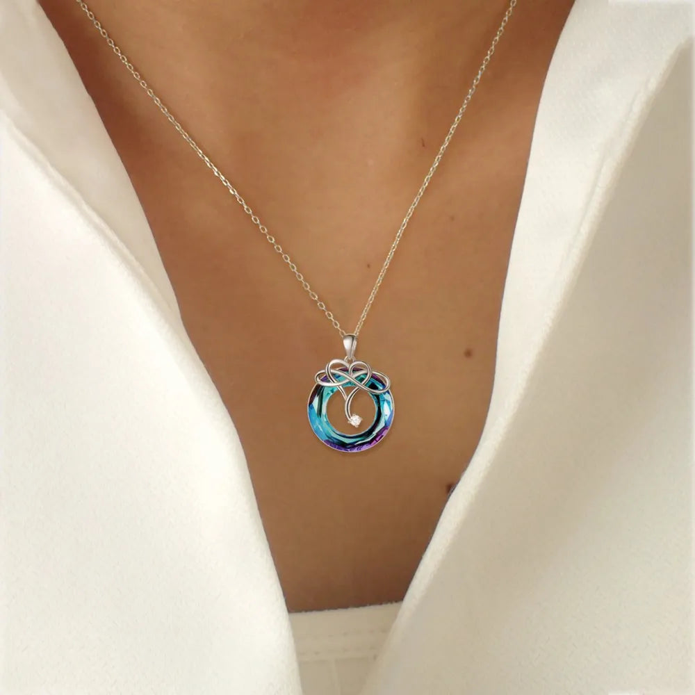 Infinity knot crystal pendant necklace in royal blue with a clear accent stone.