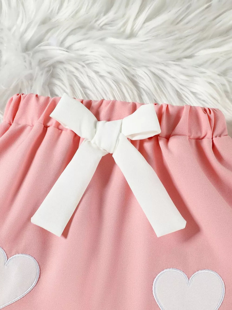 Pink baby skirt with white heart appliques and a white bow detail.