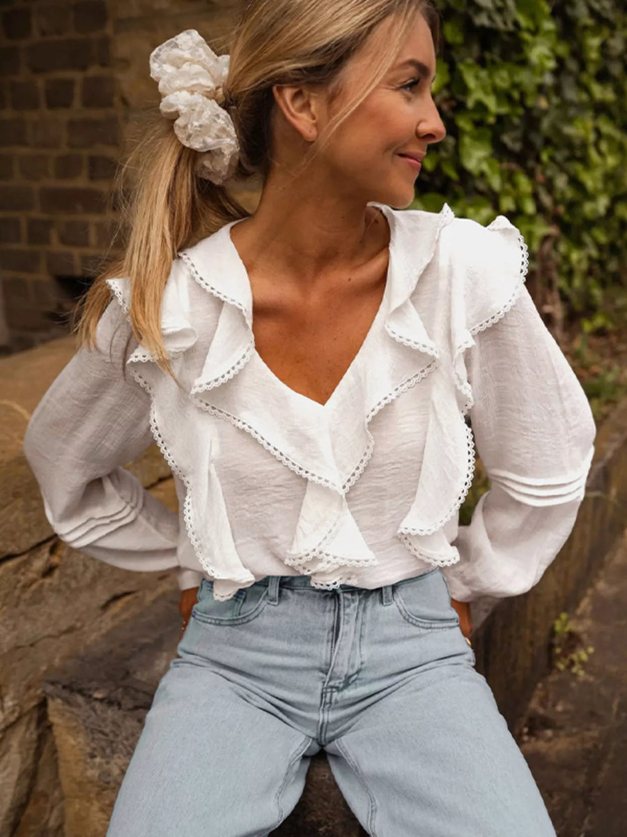 White lace ruffle v-neck blouse with long sleeves and lace trim details.