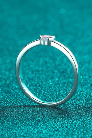 Silver ring with a heart-cut solitaire diamond on a textured teal background.