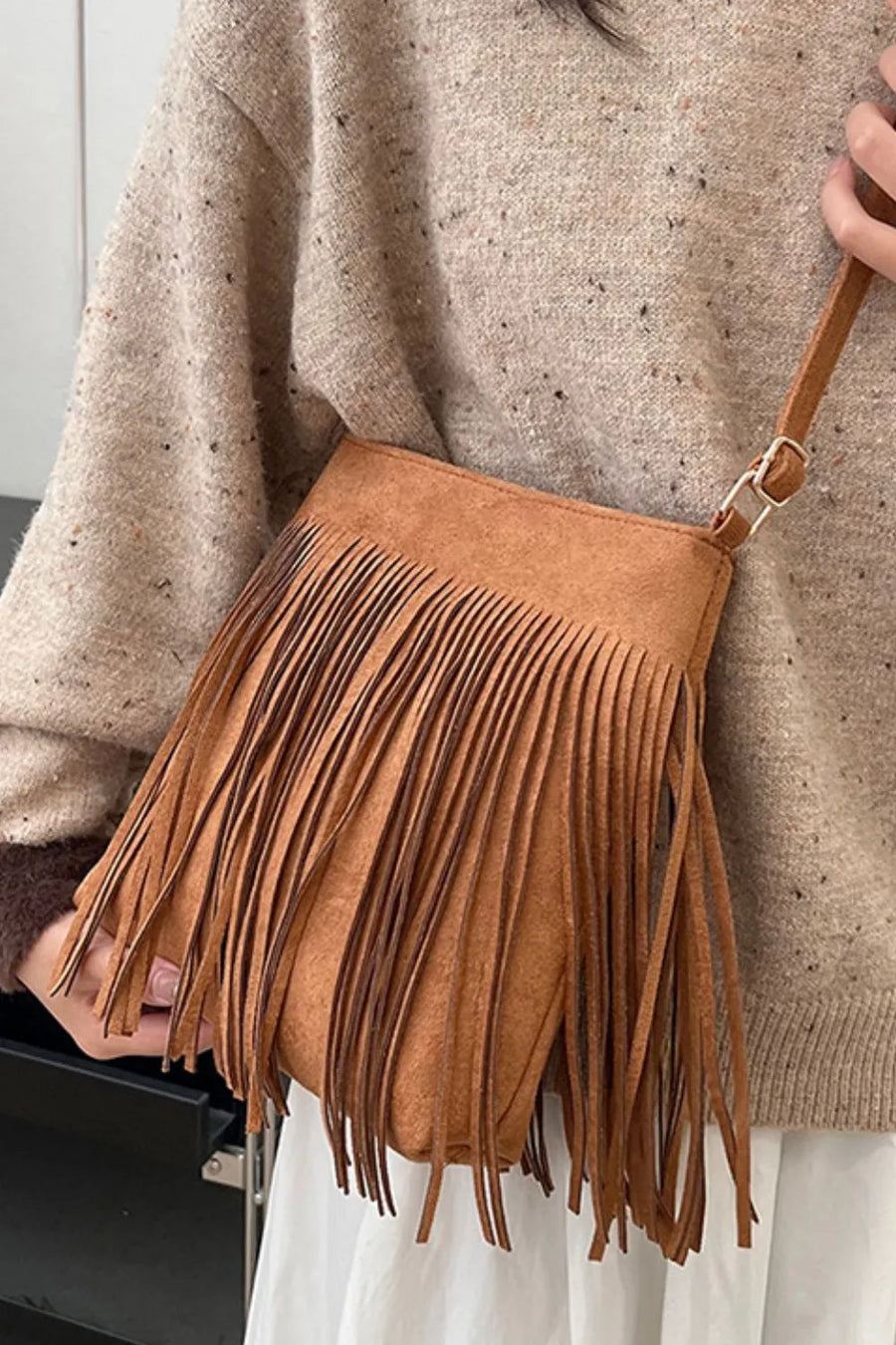 Brown suede crossbody bag with fringe detail and adjustable strap.