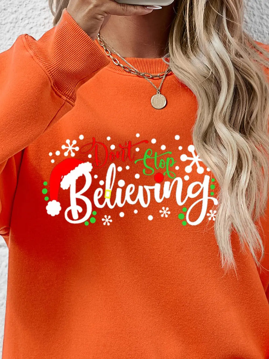 Orange long sleeve sweater with "Don't Stop Believing" graphic and Santa hat detail