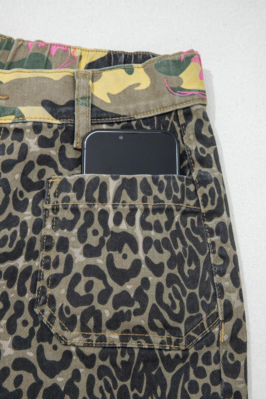 Contrast patchwork floral and leopard print jeans with camo belt detail and a phone in the pocket.