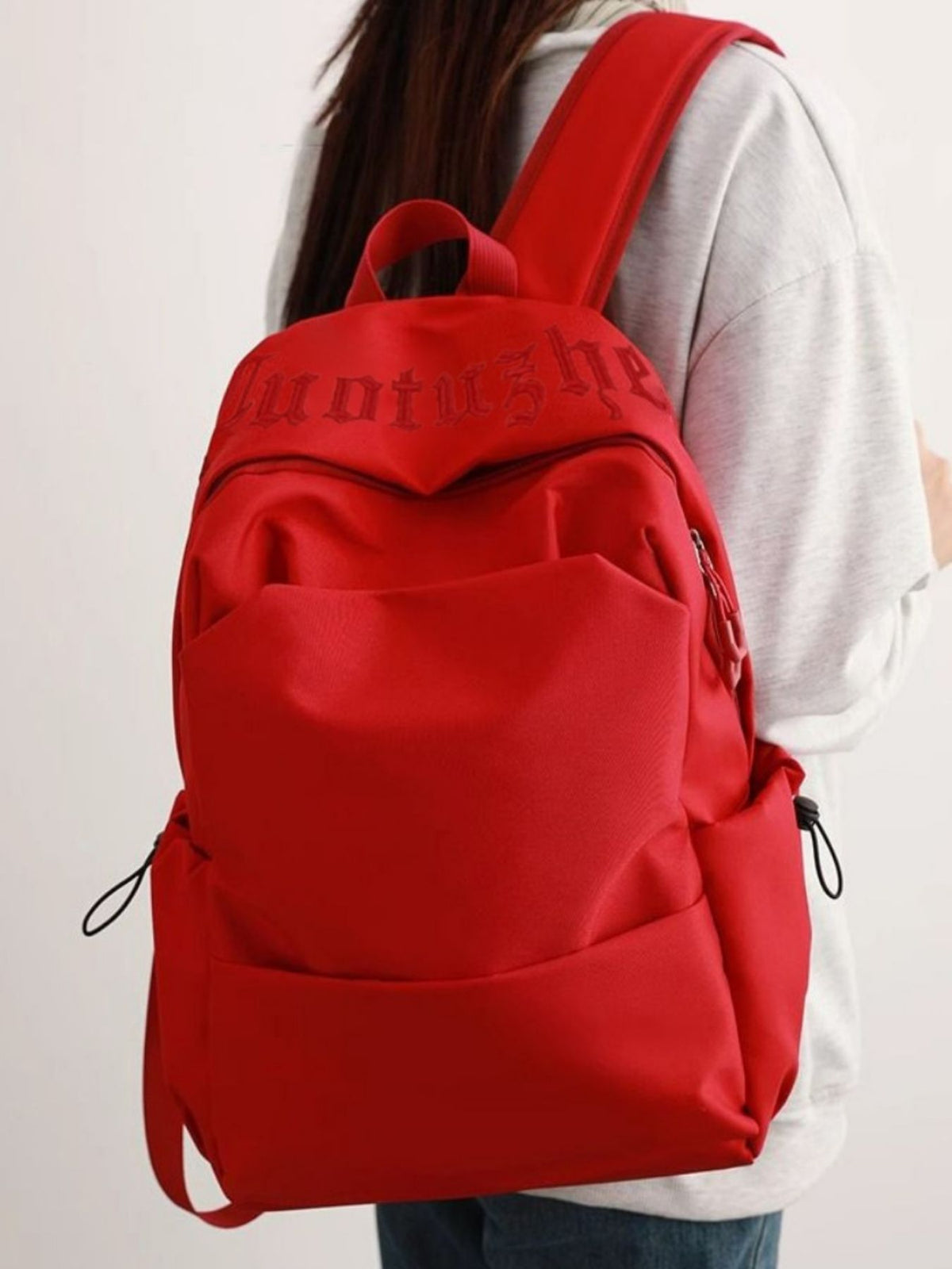 Red nylon drawstring backpack with padded straps and embroidered text detail