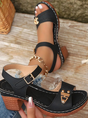 Black laser-cut detail block heel sandals with gold buckle and white stitching.