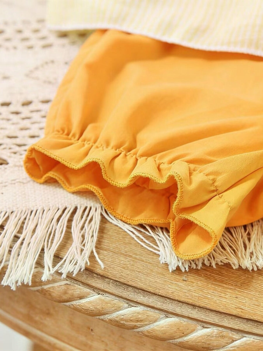 Orange baby shorts with ruffled hem and yellow striped top detail.