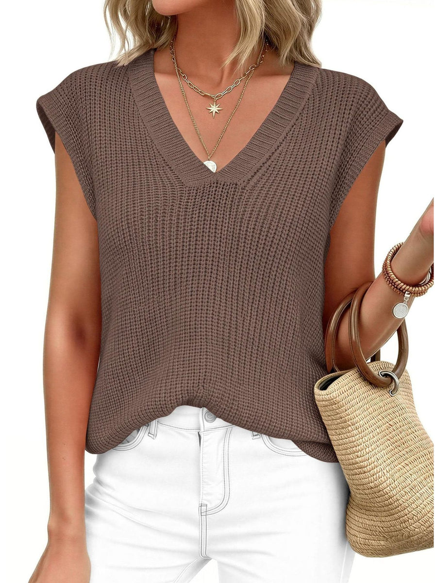 Brown textured V-neck sweater vest with cap sleeves, styled with layered necklaces and white jeans.