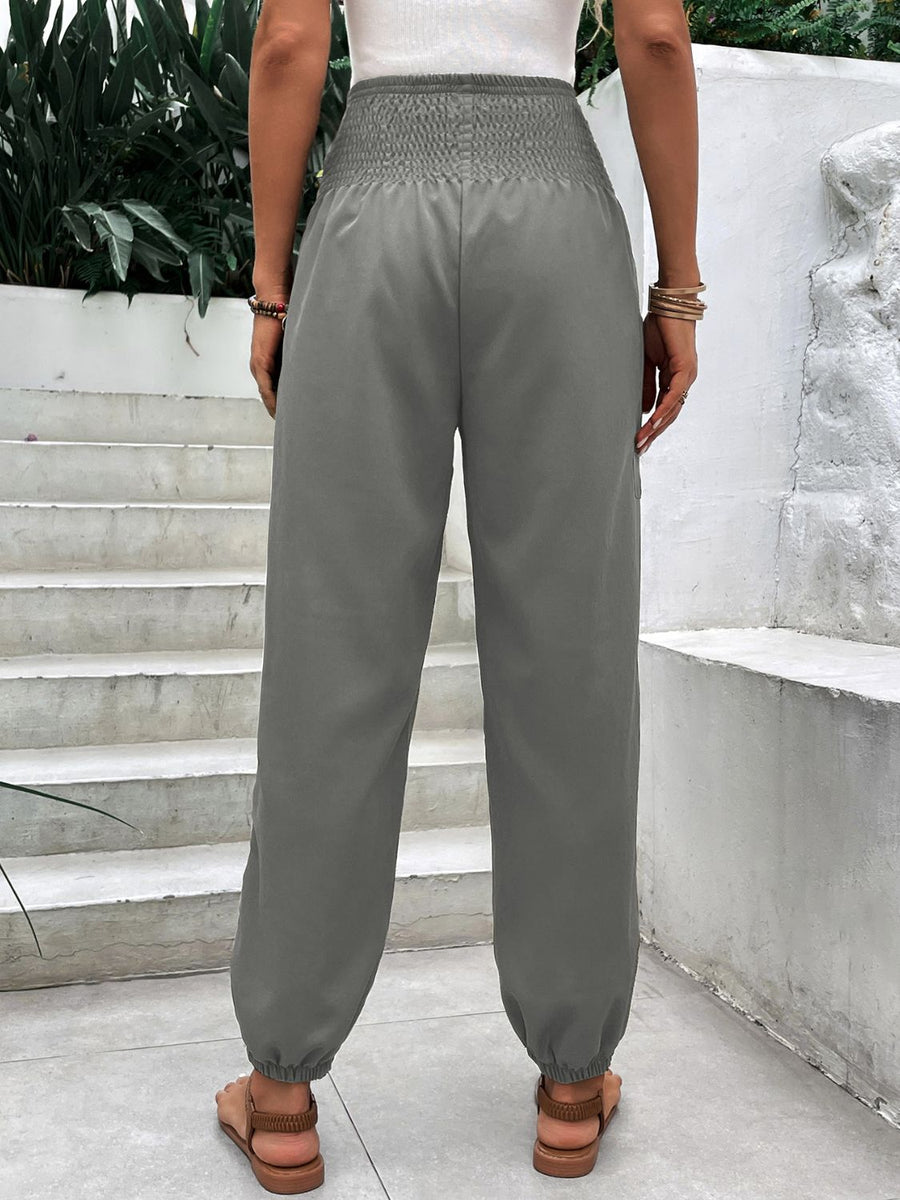 Gray relaxed-fit trousers with smocked waistline and cinched ankles.